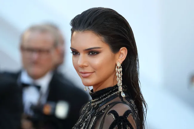Model wearing a black embellished dress with long earrings at a red carpet event.