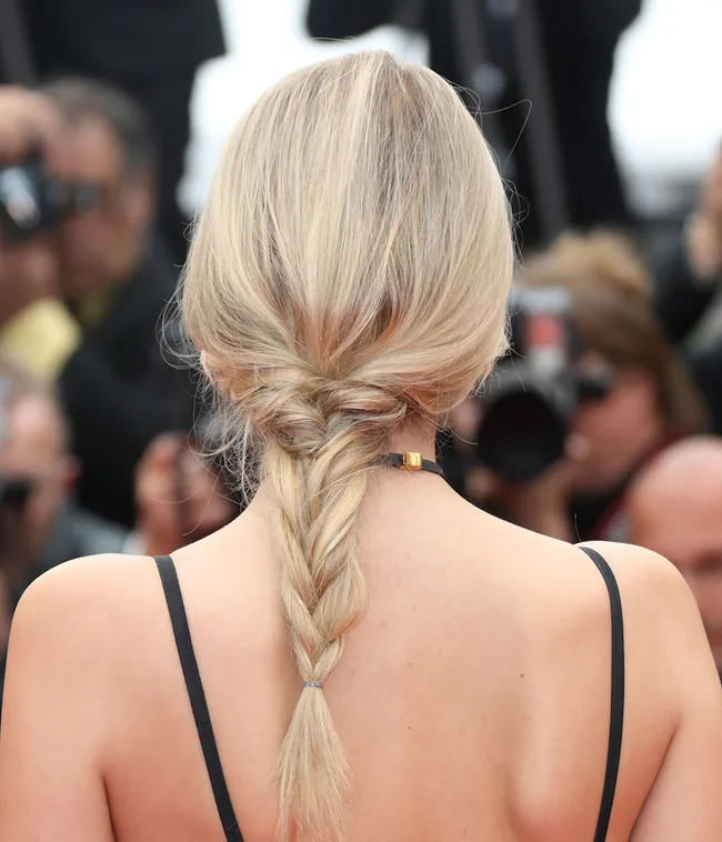 Blonde hair styled in a loose braid; person wearing a black strap dress, photographed from behind.