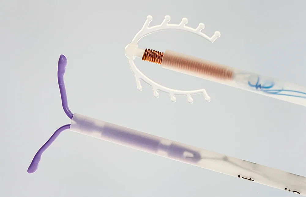 Close-up of two IUDs: a copper coil and a hormonal device with a T-shaped structure on a light background.