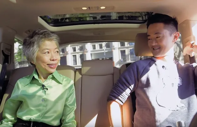 Two people sitting in a car, smiling and looking at each other. Sunlight filters through the windows.