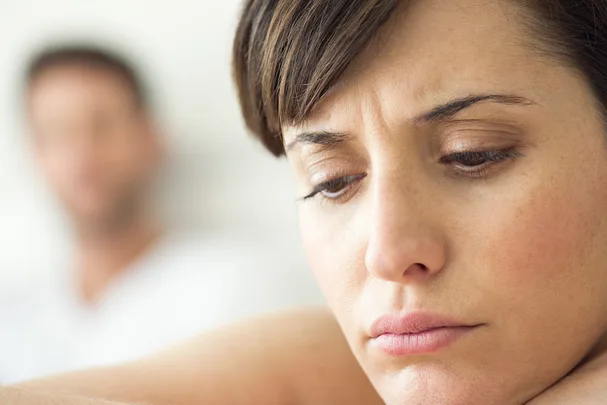 Sad woman in focus, with a blurry man in the background, conveying emotional distance or conflict.