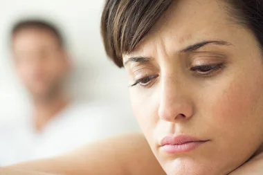 Sad woman in focus, with a blurry man in the background, conveying emotional distance or conflict.