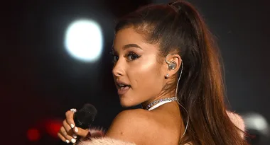 ```html
<img src="image-url.jpg" alt="Performer with ponytail sings on stage with microphone and earpiece." />
```