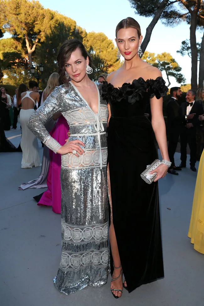 Two women in elegant evening gowns pose together outdoors at an event.