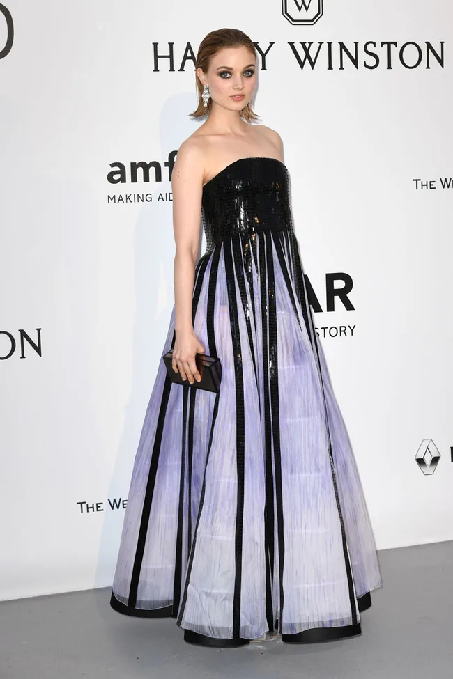 A person wearing a strapless sequined gown with vertical stripes, holding a clutch, attending a formal event.