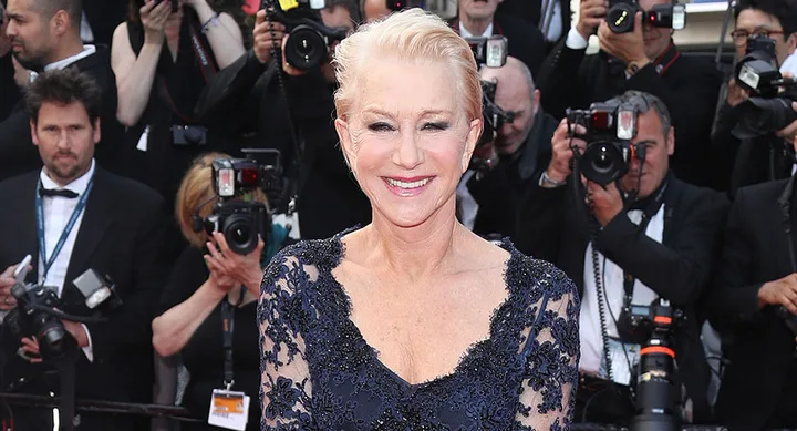 Photo of a woman in a blue lace gown smiling, surrounded by photographers on the red carpet.
