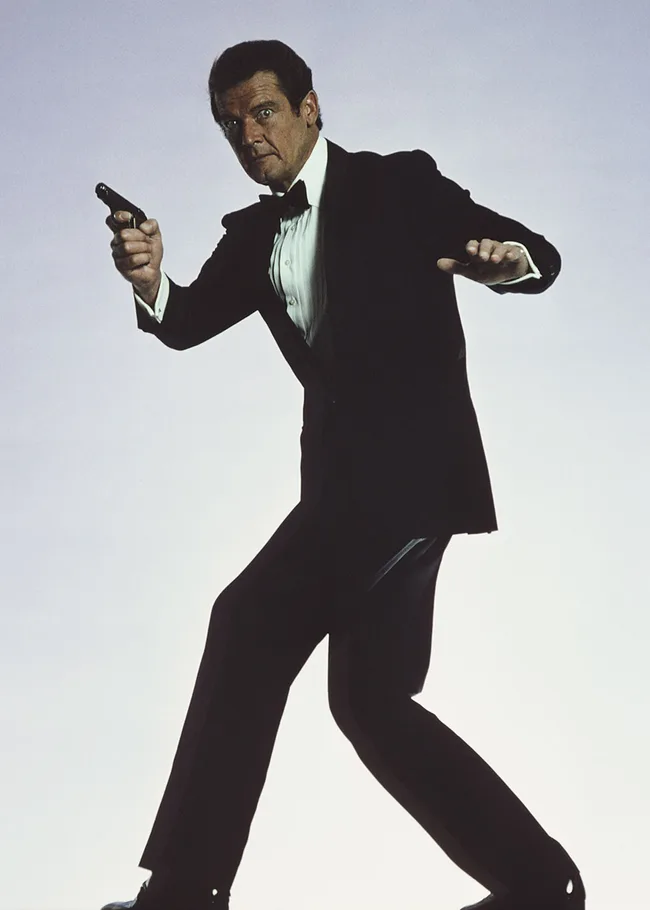 Man in a tuxedo posing with a pistol, in an action stance against a neutral background.