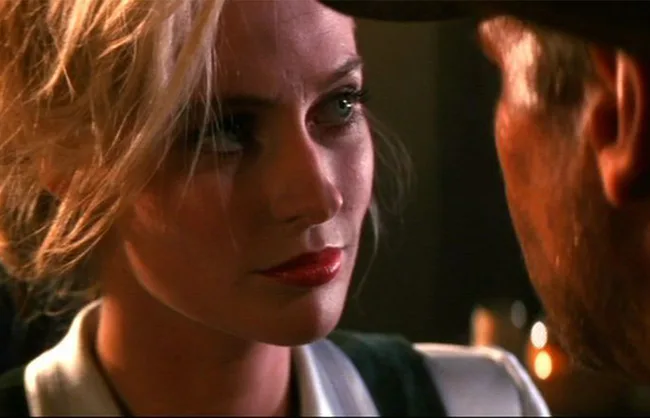 A woman with blonde hair looking intently at a man, both in a dimly lit setting.