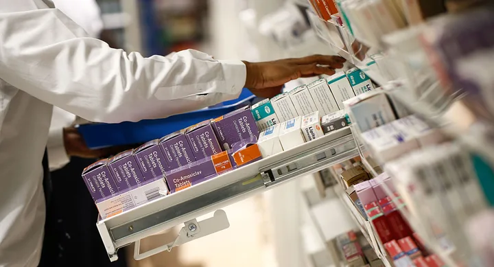Pharmacist organizing medicine boxes on a pharmacy shelf.