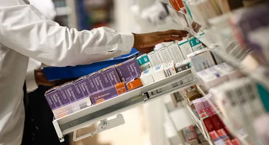 Pharmacist organizing medicine boxes on a pharmacy shelf.