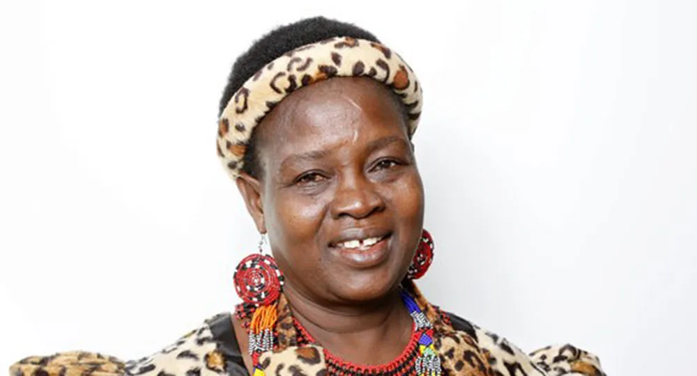 A person wearing traditional attire with leopard-patterned headband and earrings, smiling against a white background.
