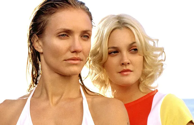 Two women standing closely, gazing in different directions, on a bright day. One has wet hair, the other has curls.