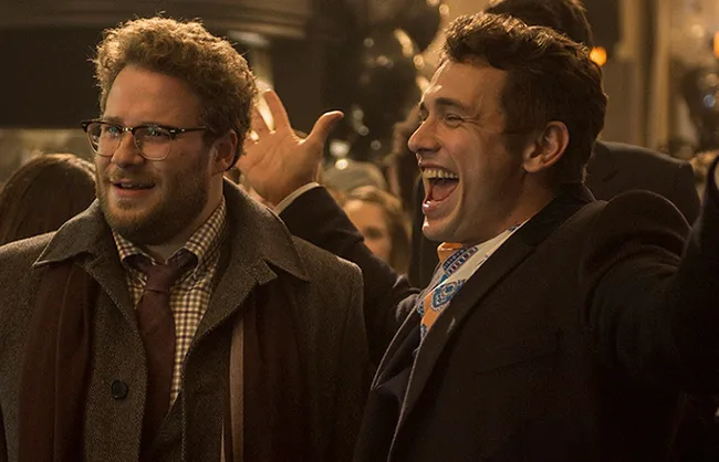 Two men in suits, one with glasses, smiling and excited at an indoor event.