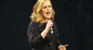 Singer in a sparkling dress passionately performing on stage with a microphone.
