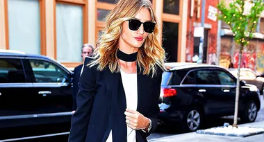 Woman with sunglasses and a black blazer walks on a city street.