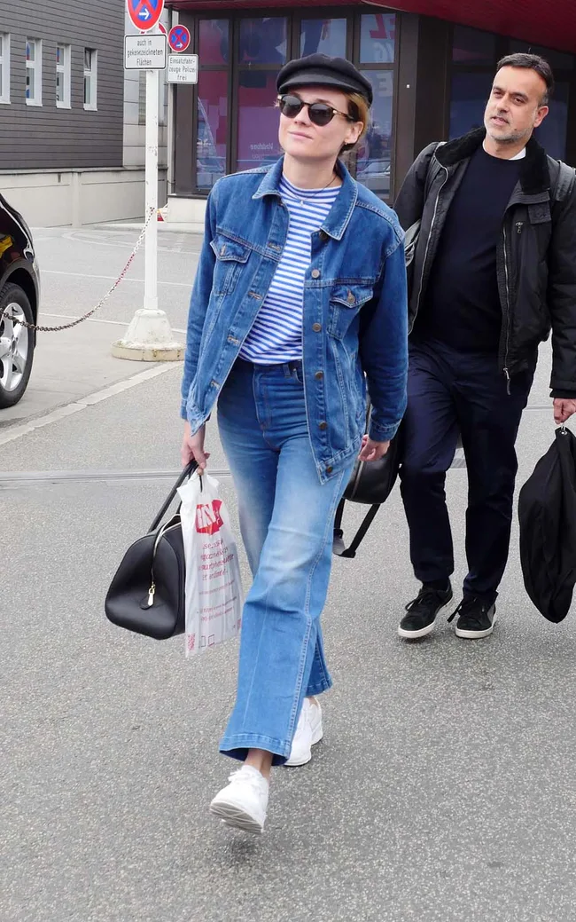 Fashionable woman in denim, striped top, black cap, and sunglasses walking with a man, holding a shopping bag.