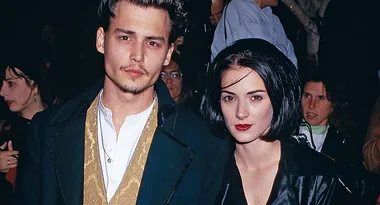 Two people posing together at a public event, one wearing a dark coat with a gold vest and the other in a black leather jacket.