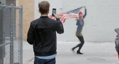 Man photographing woman waving American flag in alley.