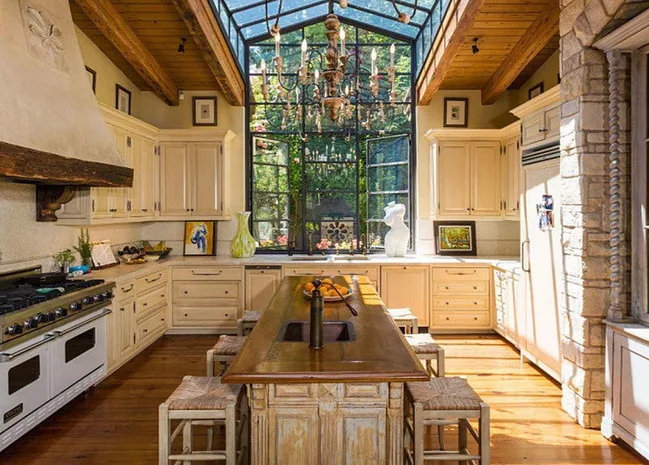 Luxurious kitchen with wooden cabinets, large island, and glass ceiling, featuring a chandelier and decorative items.