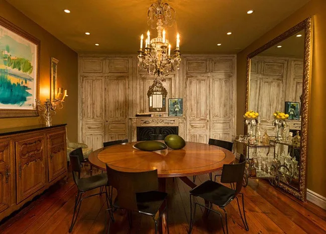 Elegant dining room with a round wooden table, chandelier, large mirror, and decorative elements in warm tones.