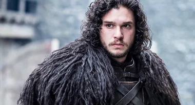 Character with curly dark hair wearing a fur cloak, standing outside in a snowy setting.