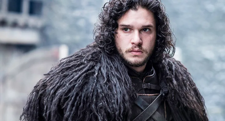 Character with curly dark hair wearing a fur cloak, standing outside in a snowy setting.