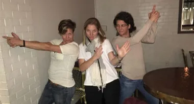 Three people posing playfully with finger guns in a casual setting.
