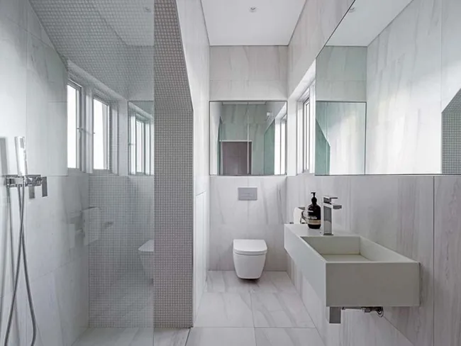 Modern minimalist bathroom with large mirrors, floating sink, shower area, and natural light from the windows.