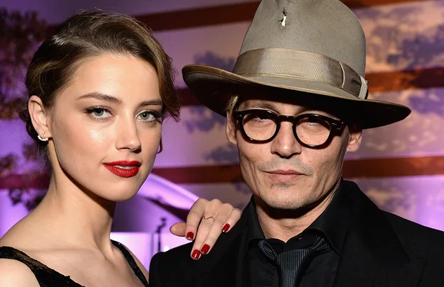 Two individuals posing closely; one wearing a hat and glasses, the other with red lipstick and earrings.