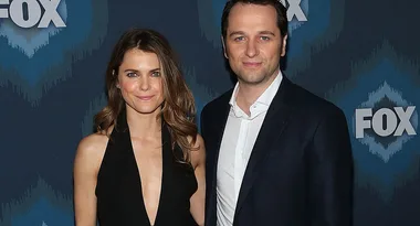 Two people posing together in front of a Fox logo backdrop at a media event.