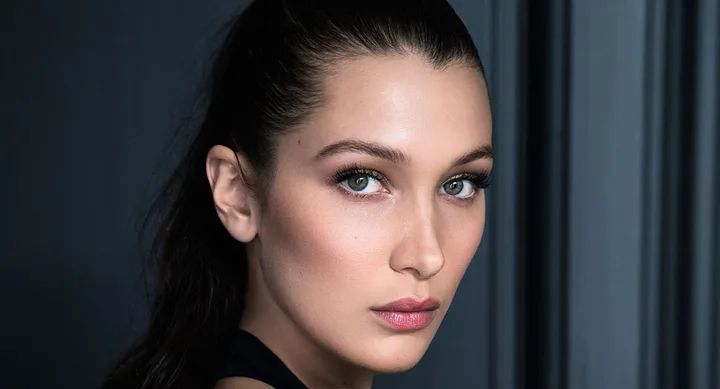 ```plaintext
Close-up of a woman with dark hair pulled back, looking directly at the camera against a dark background.
```