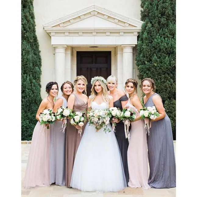 Bridal party with six bridesmaids in pastel dresses, posing outside with bouquets.