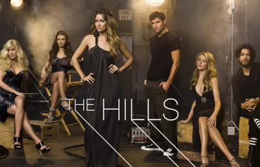 Cast of "The Hills" posing in a dimly lit studio setting with lighting equipment in the background.