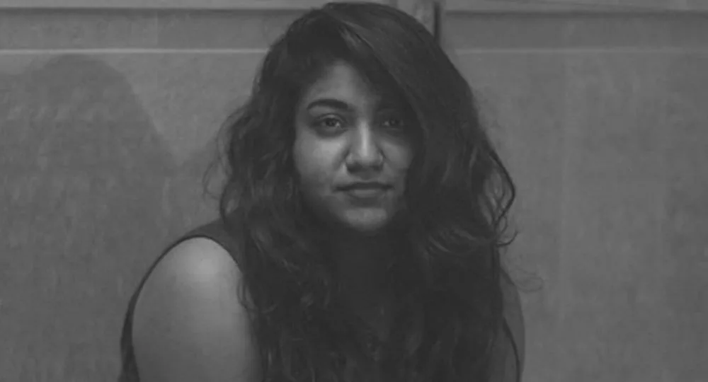 Young woman with long hair sitting, staring at the camera in a monochrome photo.