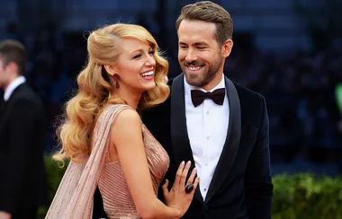 A smiling couple, dressed formally, attends an event on a red carpet. They appear happy and engaged with each other.