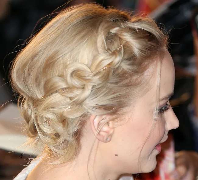 Blonde woman with an intricate braided updo hairstyle, side view.