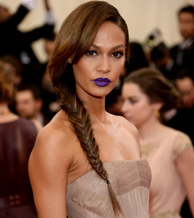 A woman with long fishtail braid and purple lipstick in a strapless dress at a formal event.