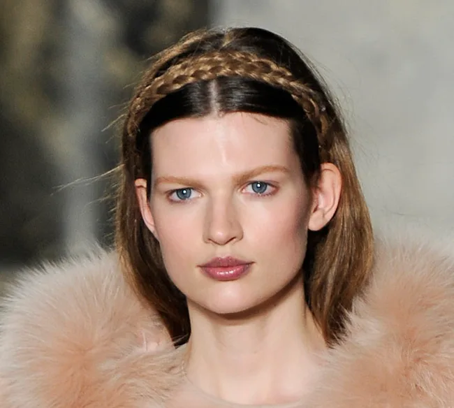 Model with braided headband wearing a fur outfit on the runway.