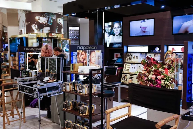 Makeup store interior with displays, director's chairs, and a flower arrangement; person with pink hair seen browsing.