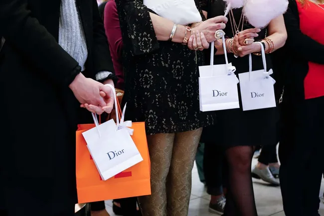 People holding Dior and orange shopping bags at an event, wearing fashionable clothes and accessories.