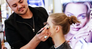 Makeup artist applying makeup to a woman's face in a beauty store setting.
