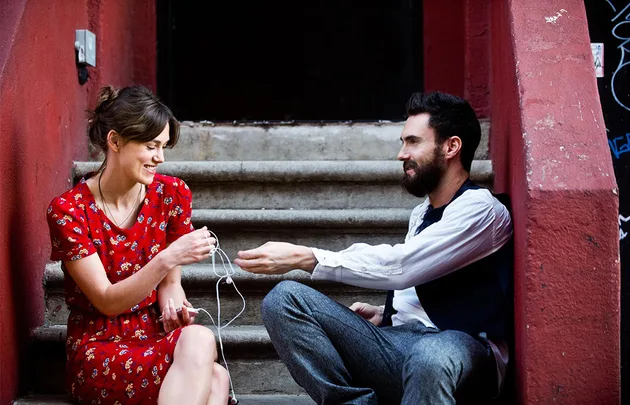 Two people sitting on steps, sharing earphones and smiling at each other.