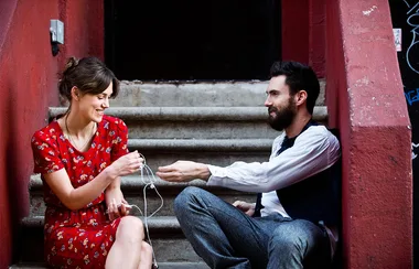 Two people sitting on steps, sharing earphones and smiling at each other.