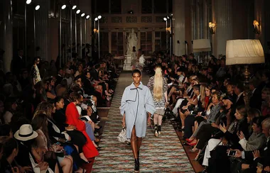 Model walking down a crowded fashion runway in a stylish outfit.