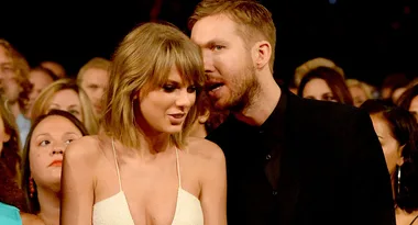 A man whispers to a woman wearing a white dress in a crowded event setting.