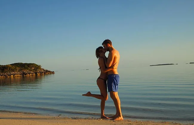 Couple embracing on a serene beach with calm waters and a clear sky.