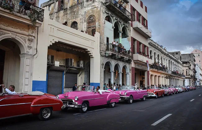 Vintage cars in pink and red parked along the street in front of historic buildings, Havana, Cuba.