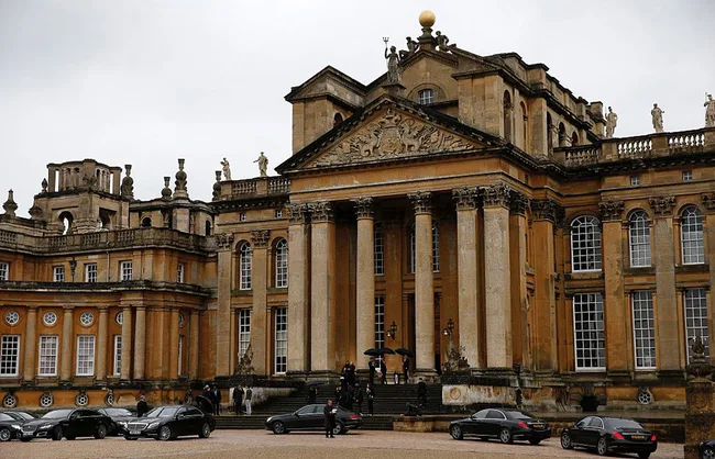 Blenheim Palace's grand entrance with cars parked in front, showcasing its baroque architectural style.