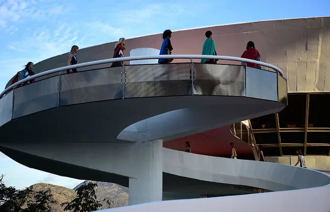 Fashion models walking on a modern, spiral walkway with a clear sky background.