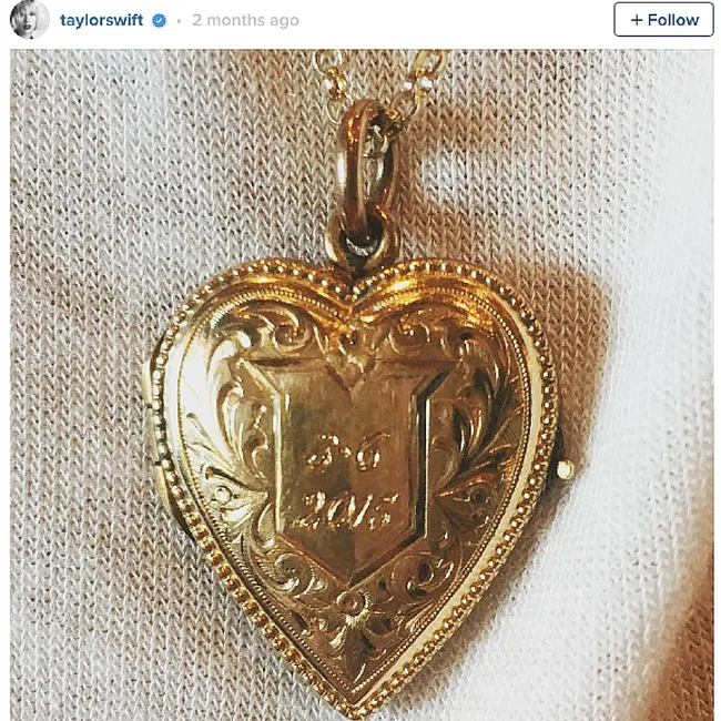 Heart-shaped gold locket necklace engraved with "23" and "2015" on a textured white background.